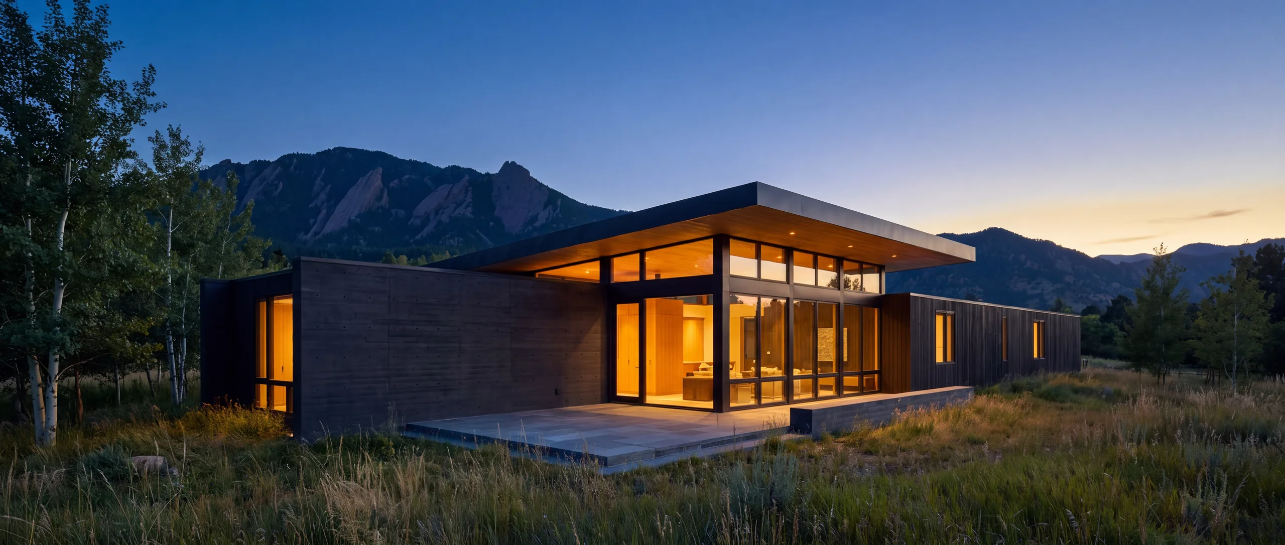 Mountain-modern Colorado luxury home glowing at dusk with the Flatirons rising behind it