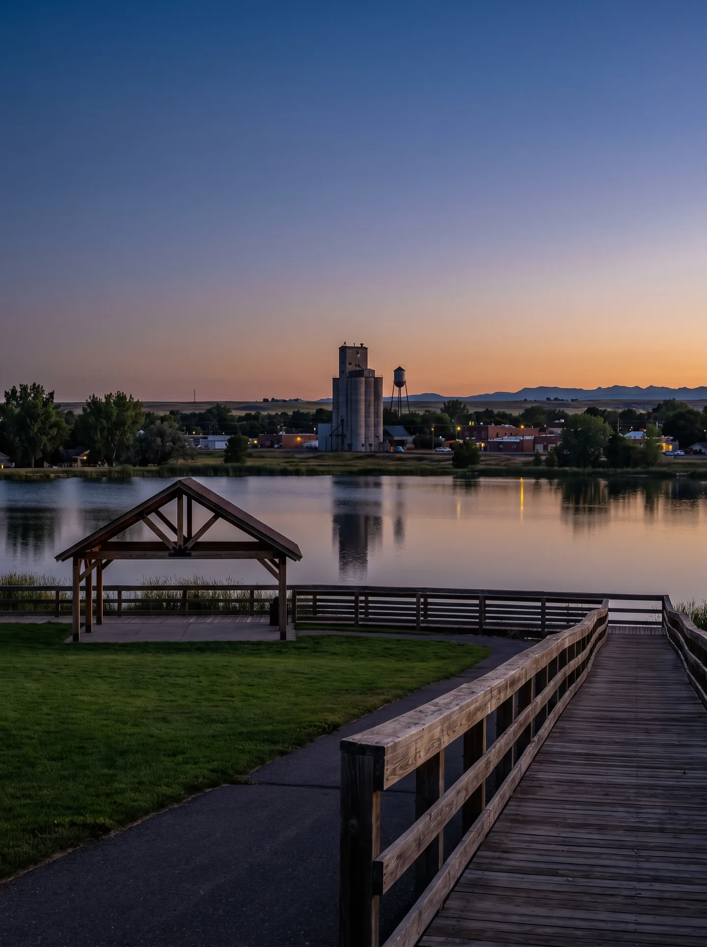 The boardwalk and pavilion at Boardwalk Park in Windsor, Colorado, looking across Windsor Lake to the historic grain elevator at dusk